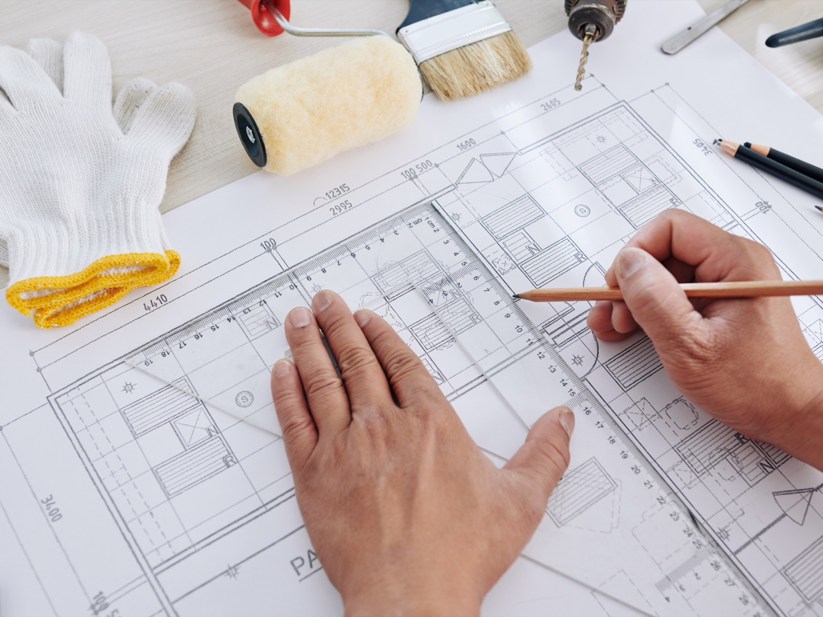 Hands finishing a house blueprint to plan a remodel budget